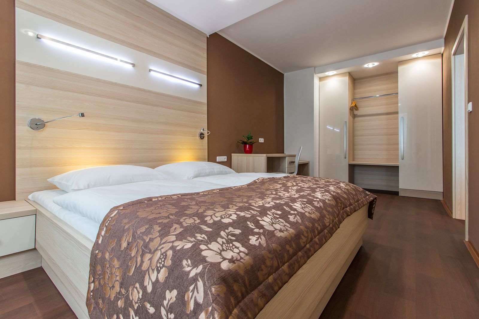 Wellness apartmán – manželská postel s hnědým přehozem a čtecími lampami na stěně